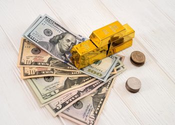 一张新木桌上放着美钞、硬币、闪闪发光的金条