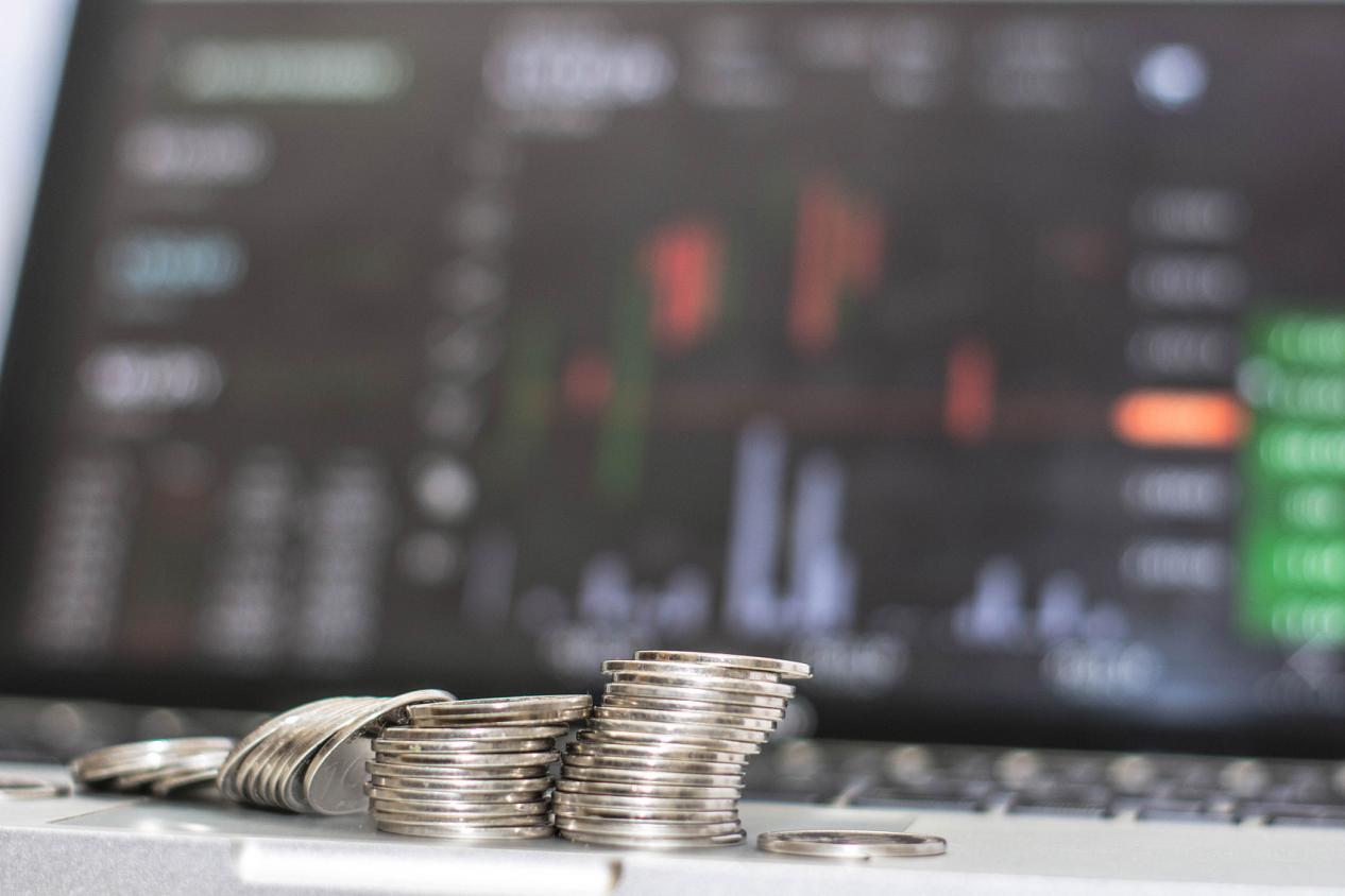 close up of silver coin in top of laptop and in front of monitor showing trading cart graphic